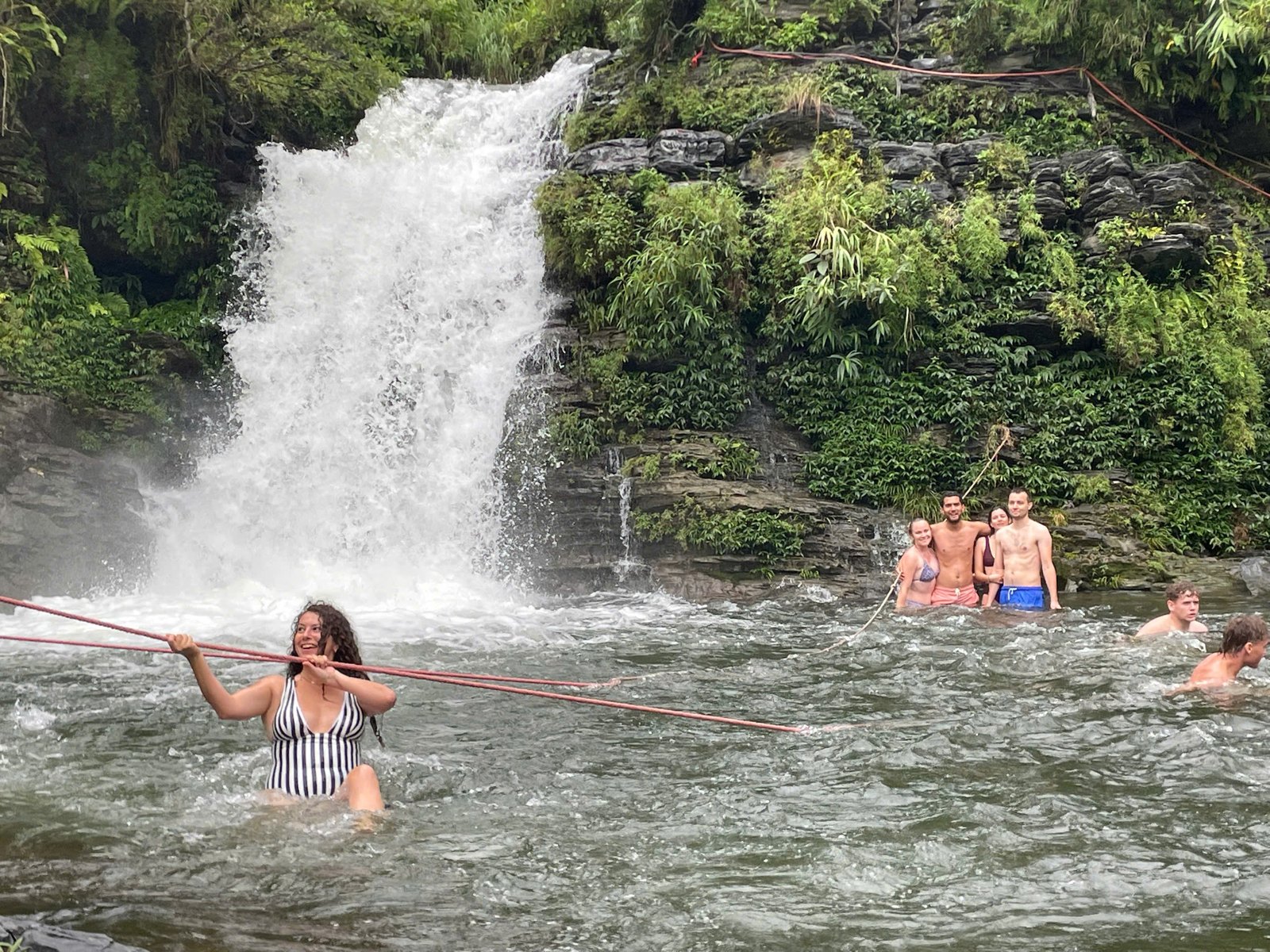 Guests swimming below a full summer waterfall on the 4-day Ha Giang Loop in August