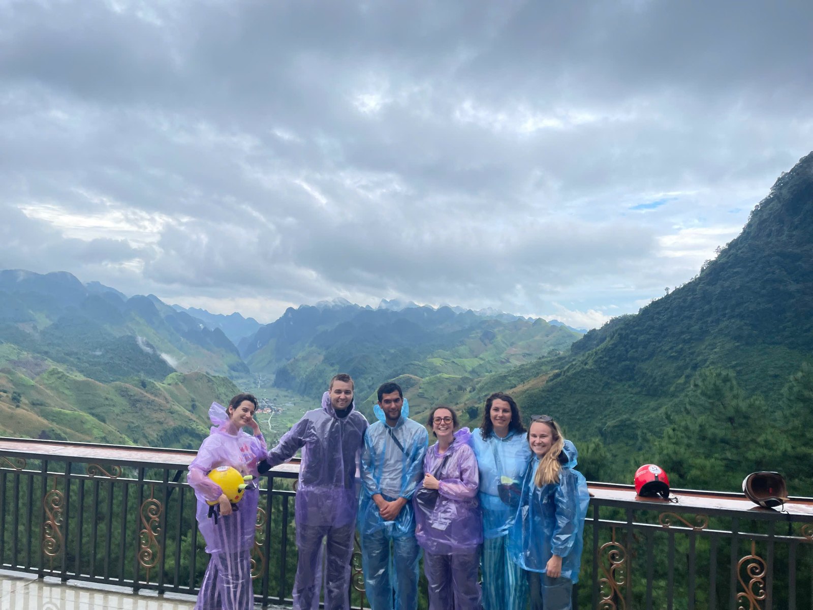 Ali tour group in raincoats at a viewpoint on the Ha Giang Loop in August as a summer storm approaches