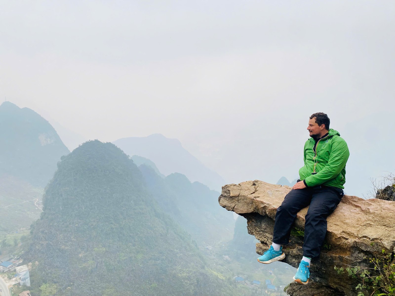 Ha Giang Loop solo traveller sitting on a rock ledge above misty karst mountains