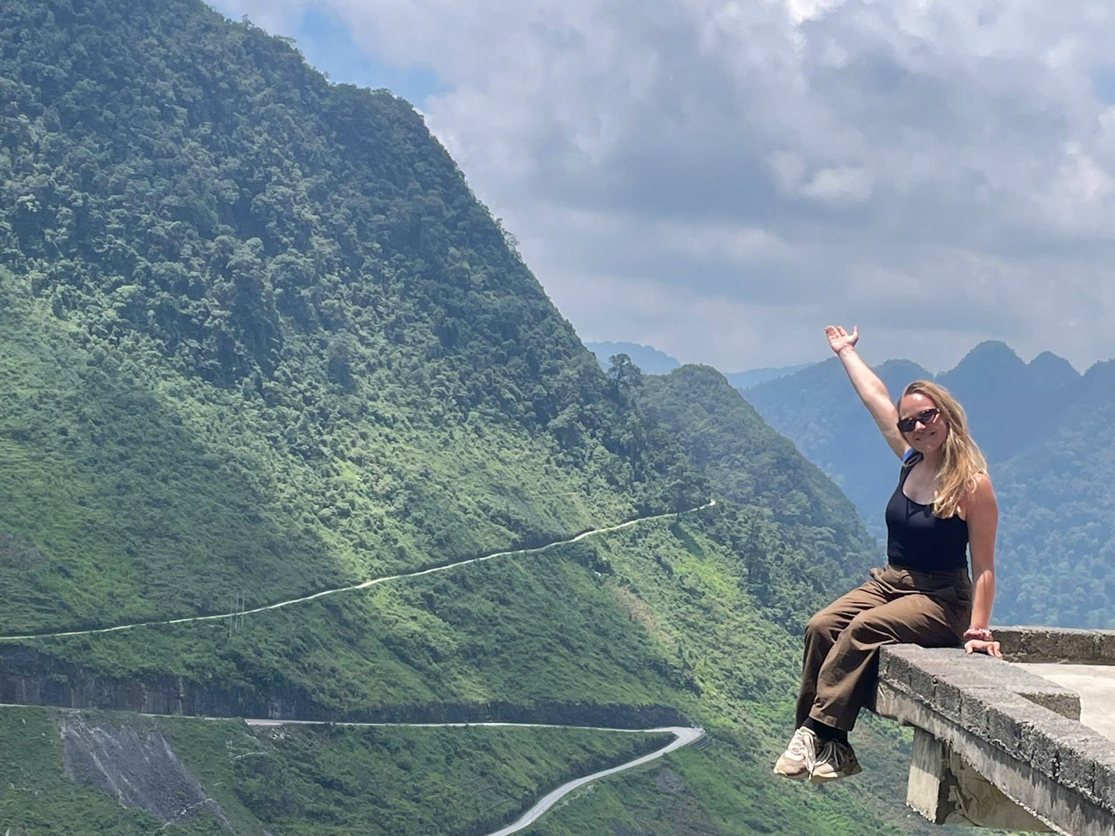 Ha Giang Loop solo female traveller waving from a viewpoint above a green mountain pass