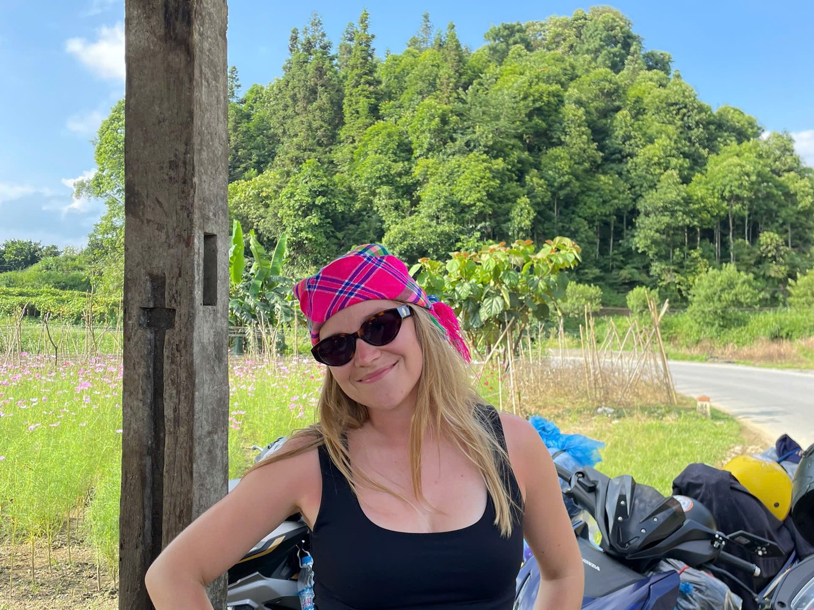 Solo female traveller smiling beside the group's motorbikes at a roadside stop