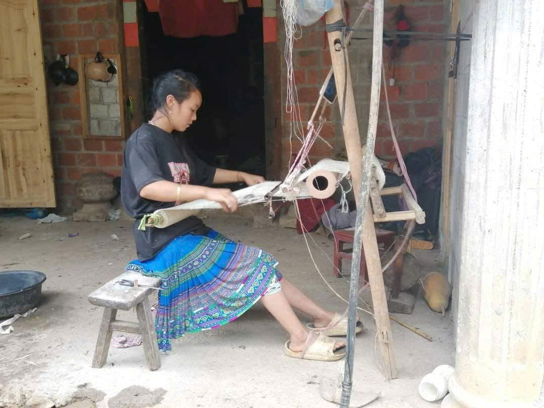 Young Hmong woman working hemp thread on a loom outside her home in Lung Tam